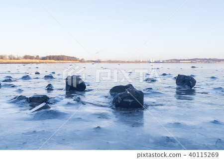 Black rocks in the ice on a frozen lake 40115269