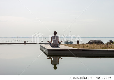 women on seaside meditating in yoga pose 40127726