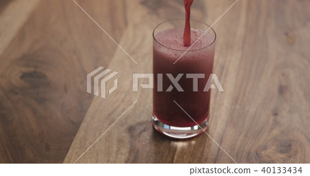 closeup pour red berry drink into a glass on wood table 40133434