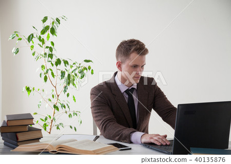 a man in a business suit works at the computer with books in the Office a man in a business suit works at the computer with books in the Office 40135876