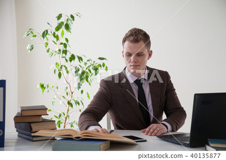 a man in a business suit works at the computer with books in the Office a man in a business suit works at the computer with books in the Office 40135877