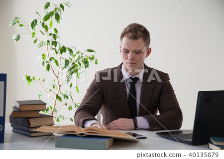 a man in a business suit works at the computer with books in the Office a man in a business suit works at the computer with books in the Office 40135879