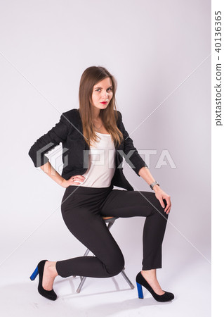 Full length studio portrait of young business woman in black suit, high heel shoes, sitting in chair Full length studio portrait of young business woman in black suit, high heel shoes, sitting in chair 40136365
