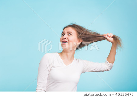 Scared young woman with unhealthy long hair keep hair in hand with nature make up portrait isolated 40136475