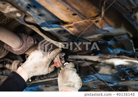 mechanic dismantles old muffler suspension on car 40138148