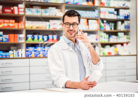 Young friendly male pharmacist with smartphone, making a phone call. Young friendly male pharmacist with smartphone, making a phone call. 40139183