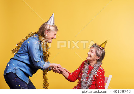 Portrait of a senior women in studio on a yellow background. Party concept. Portrait of a senior women in studio on a yellow background. Party concept. 40139743