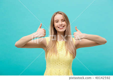 Success and Lifestyle Concept: Young happy cheerful woman showing thumb up over pastel blue Success and Lifestyle Concept: Young happy cheerful woman showing thumb up over pastel blue 40142592