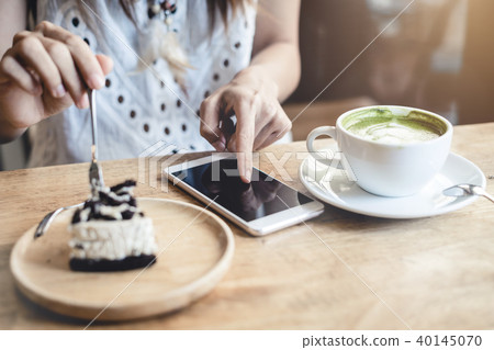 Young woman using smart phone and eating cake 40145070