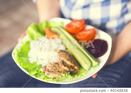 A girl holds a plate with vegetables and chicken meat with spices. 40148836