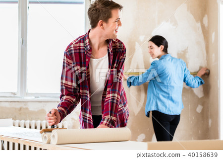 Young man applying adhesive to wallpaper while girlfriend is measuring the wall Young man applying adhesive to wallpaper while girlfriend is measuring the wall 40158639