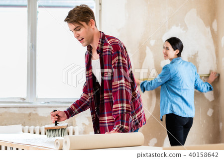 Young man applying adhesive to wallpaper while girlfriend is measuring the wall 40158642