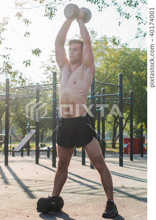 Muscular male athlete with arms raised doing lifting exercises dumbbells. 40174001