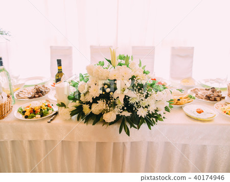 The huge white bouquet placed on the wedding table with food. 40174946