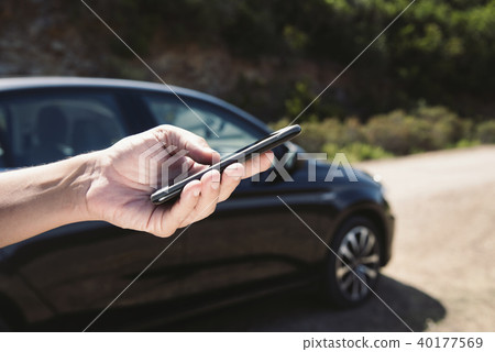 man using a smartphone next to a car on the road 40177569