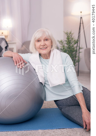 Upbeat senior woman smiling while sitting near yoga ball 40179445