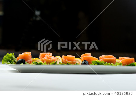 salmon snack on lettuce leaf with lemon and olives on white plate on black background 40185983