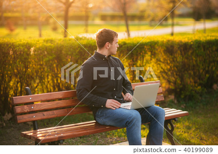 Young man sitting on the bench with laptop Young man sitting on the bench with laptop 40199089