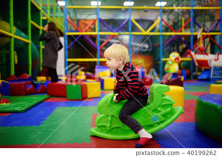 Happy little boy having fun with plastic toy-swing/hopping motorbike in play center Happy little boy having fun with plastic toy-swing/hopping motorbike in play center 40199262
