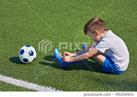 Boy football soccer tying laces him boots on grass Boy football soccer tying laces him boots on grass 40208403