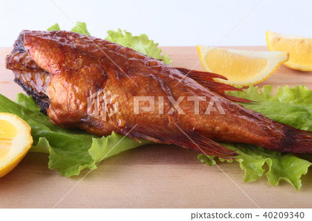 Smoked fish and lemon on green lettuce leaves on Wooden cutting board isolated on white background. Smoked fish and lemon on green lettuce leaves on Wooden cutting board isolated on white background. 40209340