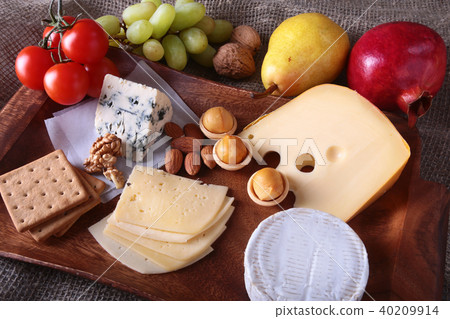 Assortment of cheese with fruits, grapes and nuts on a wooden serving tray. Assortment of cheese with fruits, grapes and nuts on a wooden serving tray. 40209914