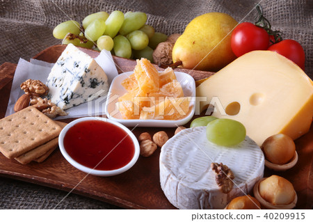 Assortment of cheese with fruits, grapes and nuts on a wooden serving tray. Assortment of cheese with fruits, grapes and nuts on a wooden serving tray. 40209915