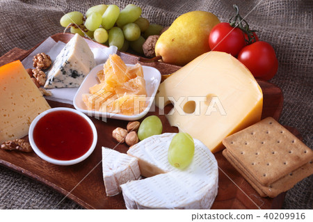 Assortment of cheese with fruits, grapes and nuts on a wooden serving tray. Assortment of cheese with fruits, grapes and nuts on a wooden serving tray. 40209916