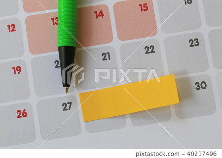 Green pen points to a twenty seven number of calendar and have blank yellow note paper. 40217496