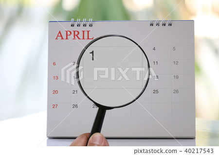 Magnifying glass in hand on calendar you can look first day of month,Focus number one in April. 40217543