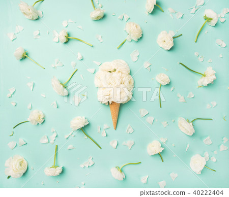 Waffle cone with white buttercup flowers over light blue background Waffle cone with white buttercup flowers over light blue background 40222404