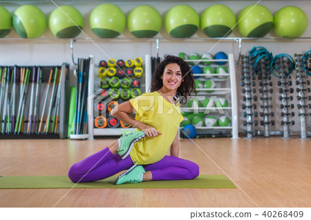 Attractive brunette young woman sitting on mat warming-up before training stretching her quadriceps 40268409