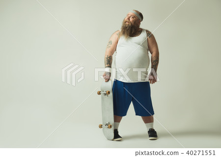 Cheerful fat man keeping skateboard and dreaming Cheerful fat man keeping skateboard and dreaming 40271551