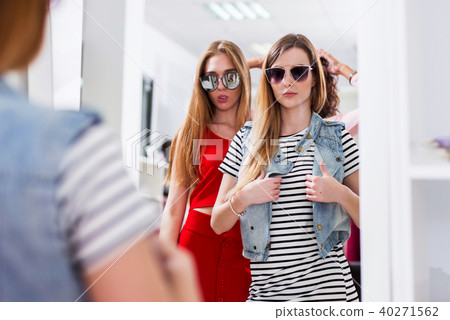 Glamorous girls trying on sunglasses posing in front of the mirror in fashion boutique Glamorous girls trying on sunglasses posing in front of the mirror in fashion boutique 40271562