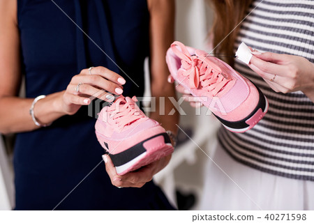 Three young girlfriends examining holding new pair of sports footwear standing in fashion showroom 40271598