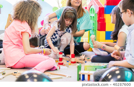 Dedicated kindergarten teacher holding a shy girl while watching children play 40287600