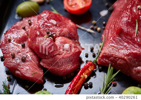 Flat lay of raw beefsteak with vegetables, herbs and spicies on metal tray, close-up, selective 40290261