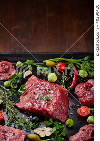 Flat lay of raw beefsteak with vegetables, herbs and spicies on metal tray, close-up, selective 40290420