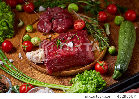 Still life of raw beef meat with vegetables on wooden plate over vintage background, top view Still life of raw beef meat with vegetables on wooden plate over vintage background, top view 40290597