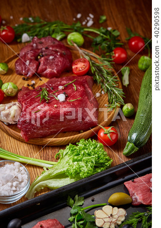 Still life of raw beef meat with vegetables on wooden plate over vintage background, top view Still life of raw beef meat with vegetables on wooden plate over vintage background, top view 40290598
