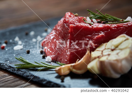 Raw meat beef steaks on black slate board with spices, garlic and rosemary over wooden background 40291042
