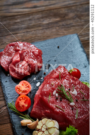 Composition of raw beefsteak on slate board with vegetables and seasoning, selective focus, close-up 40291112