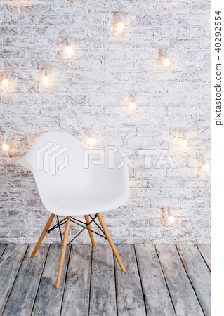 Modern white plastic chair in loft white room interior with wooden floor. Light bulbs garland on 40292554