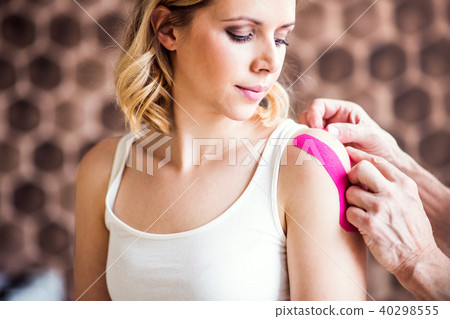 Senior male physiotherapist applying tape on a female patient. Close up. Senior male physiotherapist applying tape on a female patient. Close up. 40298555