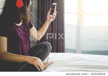 Young woman sitting in her bed and listening music in her bedroo Young woman sitting in her bed and listening music in her bedroo 40309609