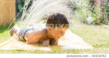 Boy cooling down with garden hose, family in the background Boy cooling down with garden hose, family in the background 40328762