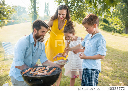 Dedicated father helping son to use wooden tongs during family picnic Dedicated father helping son to use wooden tongs during family picnic 40328772