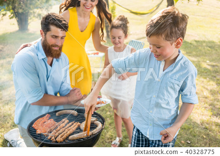 Father and son preparing meat on charcoal barbecue grill during picnic Father and son preparing meat on charcoal barbecue grill during picnic 40328775