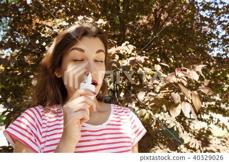 Young beautiful woman using nose spray in the park Young beautiful woman using nose spray in the park 40329026