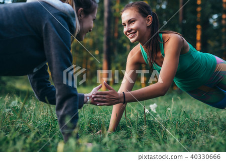 Two happy friends holding hands while doing plank exercise in park Two happy friends holding hands while doing plank exercise in park 40330666